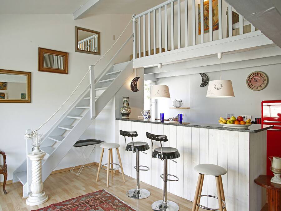 Una cocina con una escalera blanca, un frutero y tres taburetes de bar.