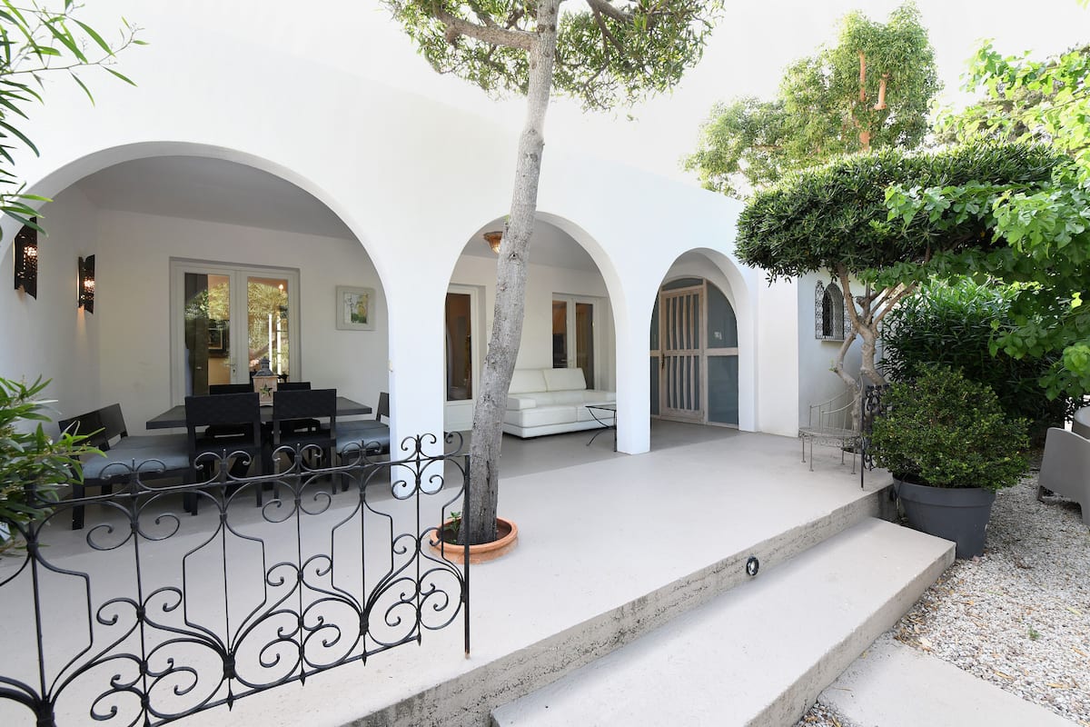 A courtyard with a dining area, white arches, and potted plants.
