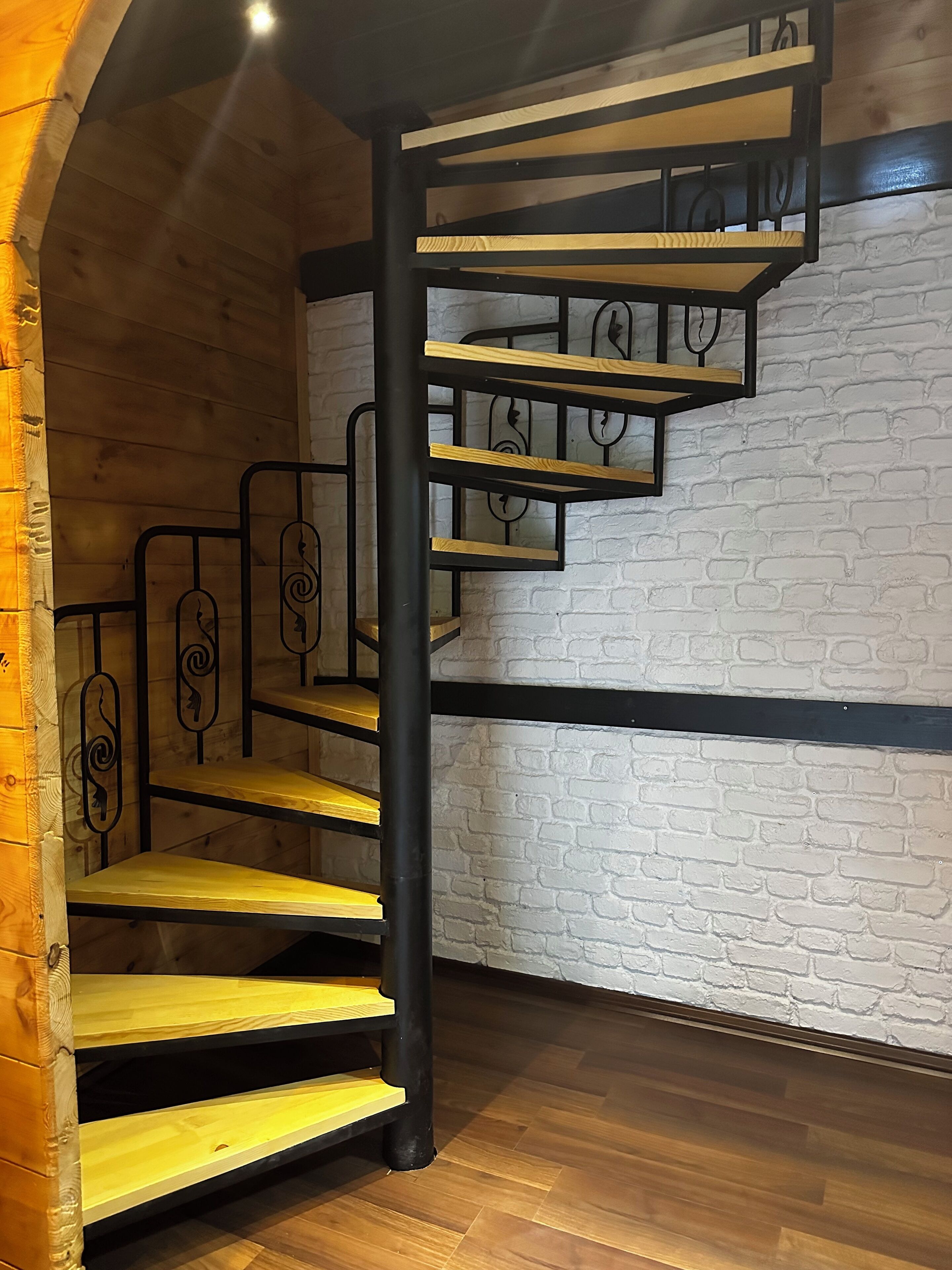 A spiral staircase with wooden steps and black metal railings, leading to an upper floor.