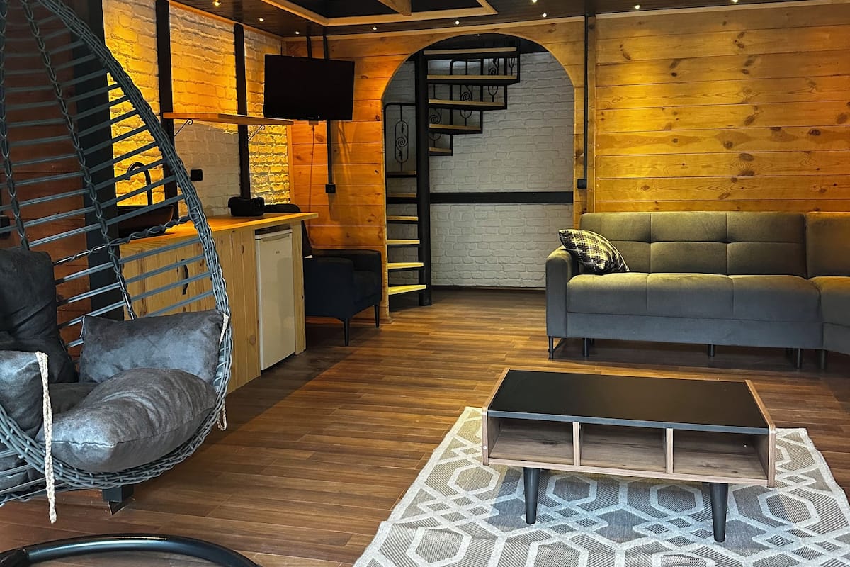Ein gemütliches Wohnzimmer mit Holzboden, einem Hängekorbstuhl, einer Couch und einer Treppe, die zu einem Erker führt.