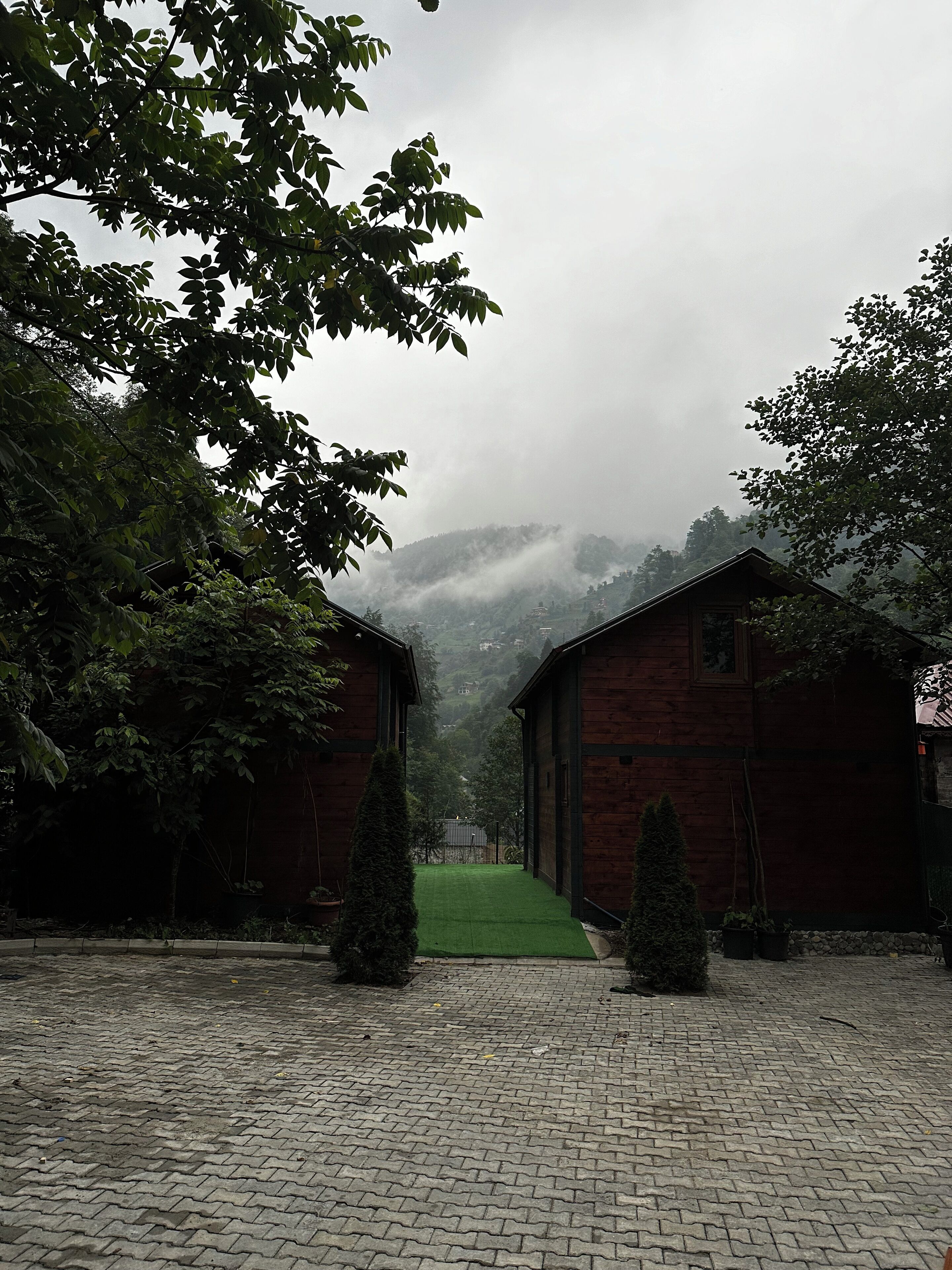A courtyard with two wooden buildings, a paved walkway, and a green lawn.