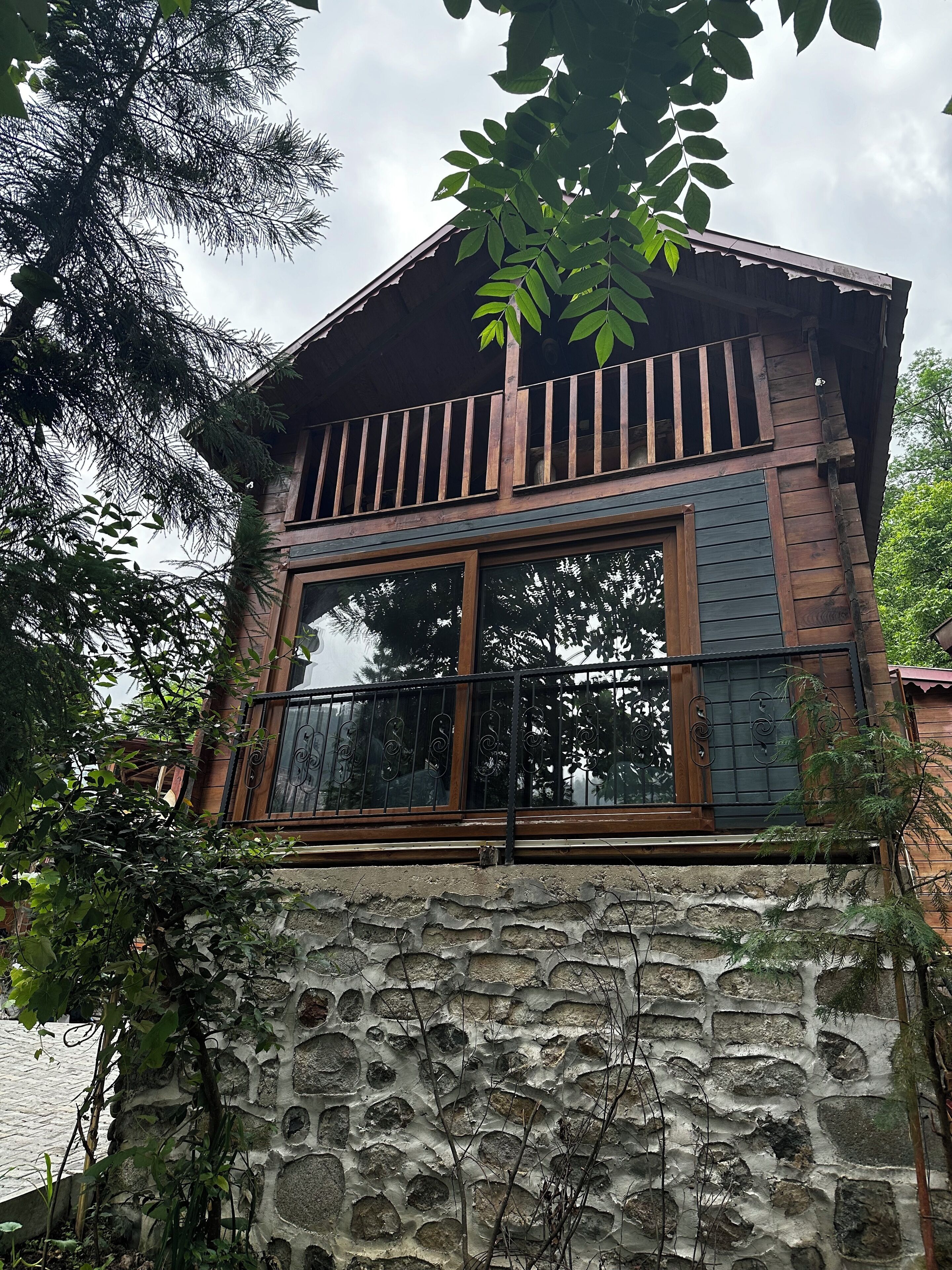 Un bâtiment de style rustique, avec une base en pierre, une structure supérieure en bois et de grandes fenêtres dotées de barreaux métalliques.