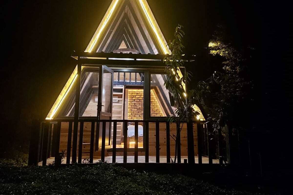 Ein dreieckiges Gebäude mit Holzfassade und Glasfront, beleuchtet durch warmes Licht.