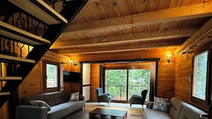 A cozy log cabin interior with a staircase, a sofa set, a coffee table, and a view of the outdoors. - Tanura Bungalows (Camlihemsin)