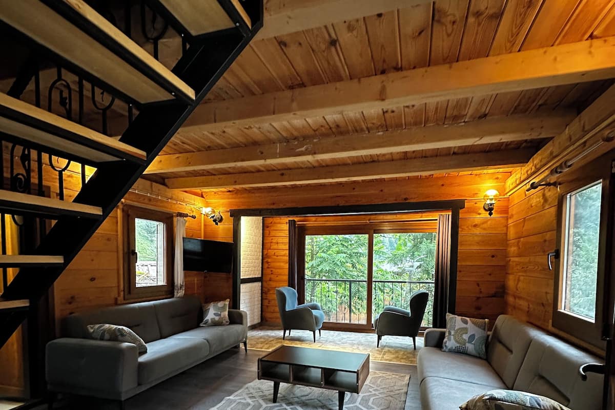 Ein gemütliches Blockhaus-Interieur mit Treppe, einer Sofagarnitur, einem Couchtisch und Blick ins Freie.