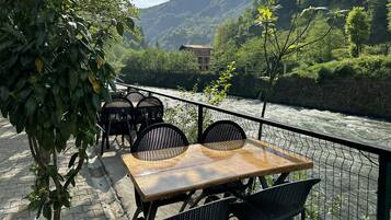 An outdoor seating area with a table and chairs, overlooking a river and a mountainous landscape.