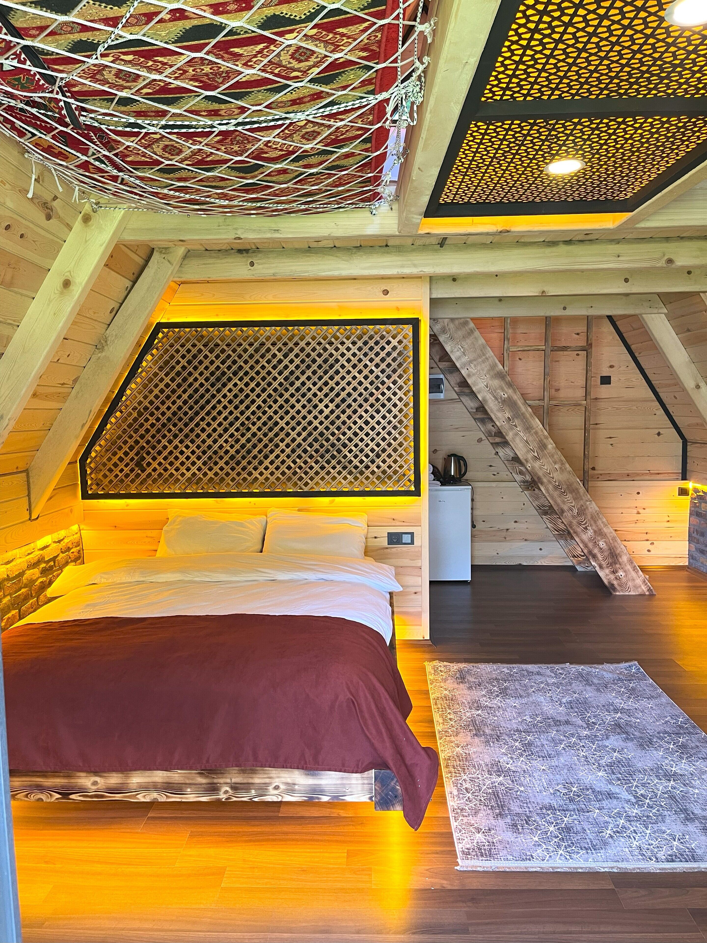 A cozy attic bedroom with a bed, wooden beams, a sloped ceiling, and a patterned wall.
