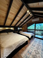 Un dormitorio con dos camas, vigas de madera en el techo, un ventanal y vistas al exterior.