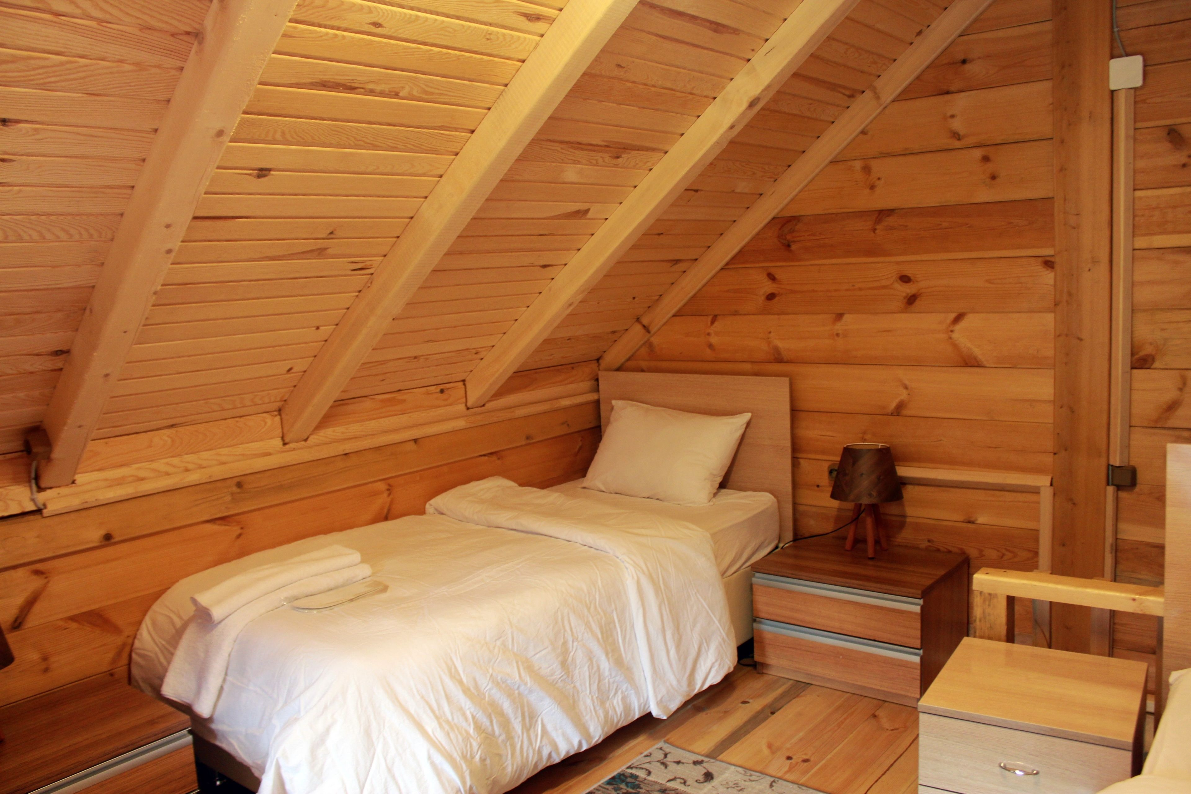A cozy wooden cabin room with a loft bed, a small bedside table, and a nightstand.