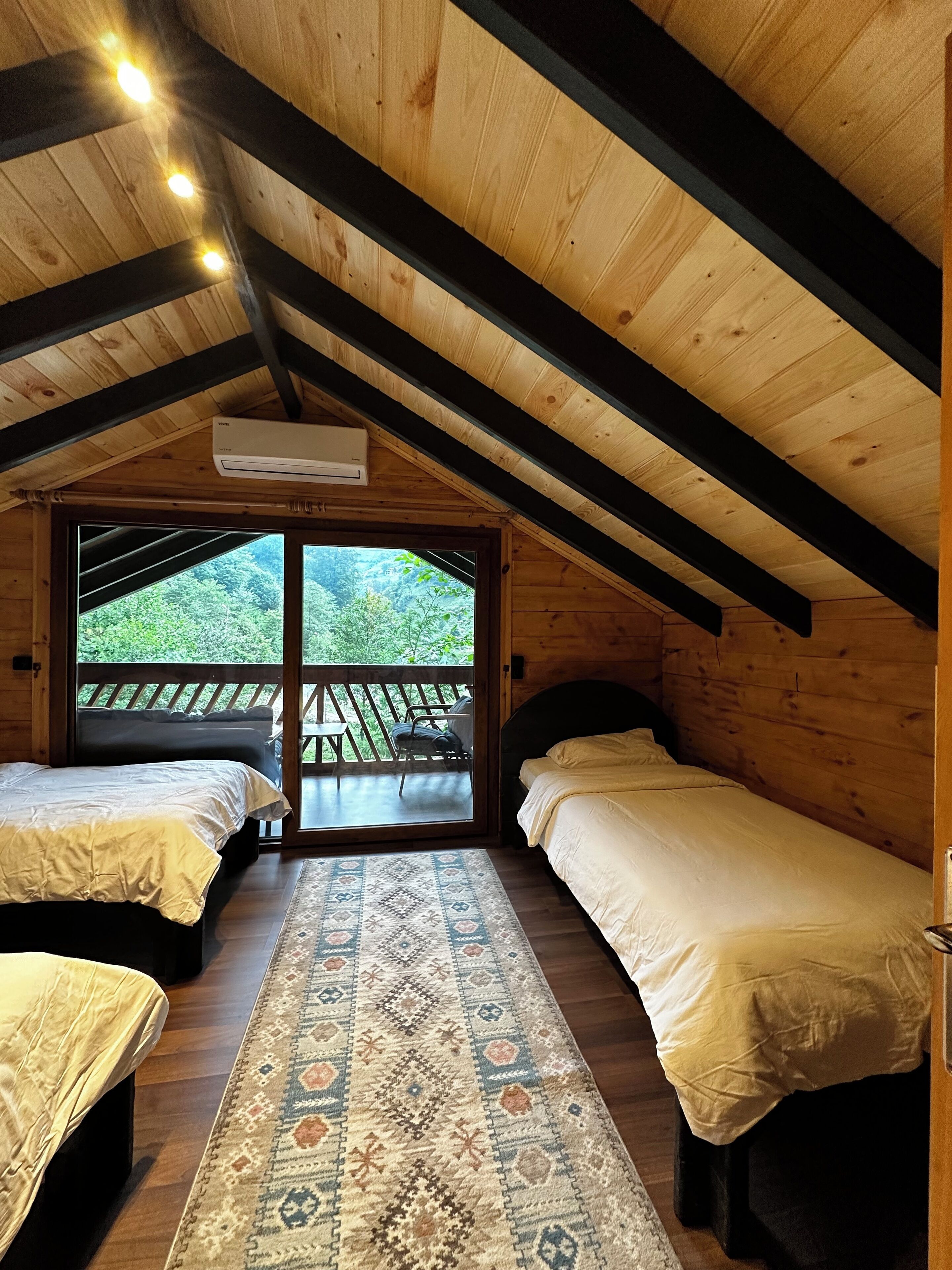 Une cabine avec deux lits, un tapis à motifs et une vue sur la verdure grâce à de grandes fenêtres.