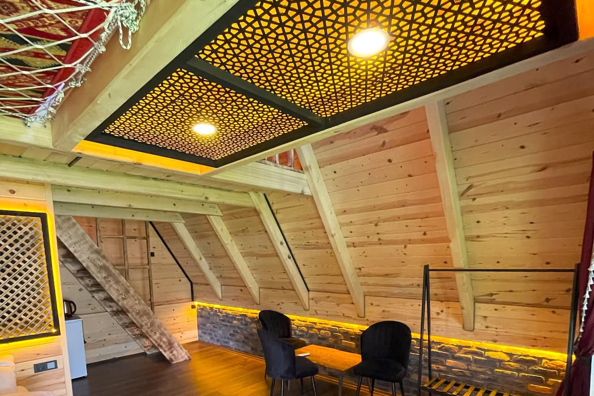 Ein gemütliches Dachzimmer mit Holzwänden, geneigter Decke und einer Sitzecke mit Stühlen und Tisch.