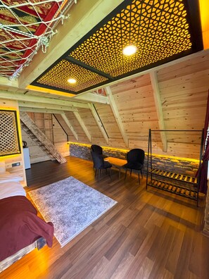 Une pièce mansardée chaleureuse avec des murs en bois, un plafond en pente et un coin salon comprenant des chaises et une table.