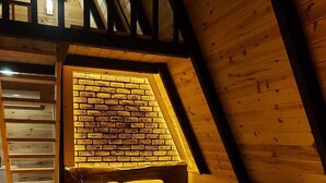 A cozy attic bedroom with a sloped ceiling, a brick wall, and a wooden bed. - Tanura Bungalows (Camlihemsin)