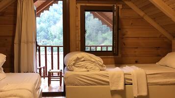 A cozy cabin with two beds, a wooden ceiling, and a large window overlooking a forest.