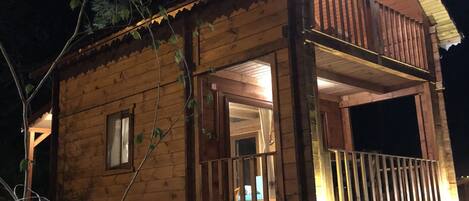 A wooden cabin with a stone foundation, a balcony, and a lit entrance.