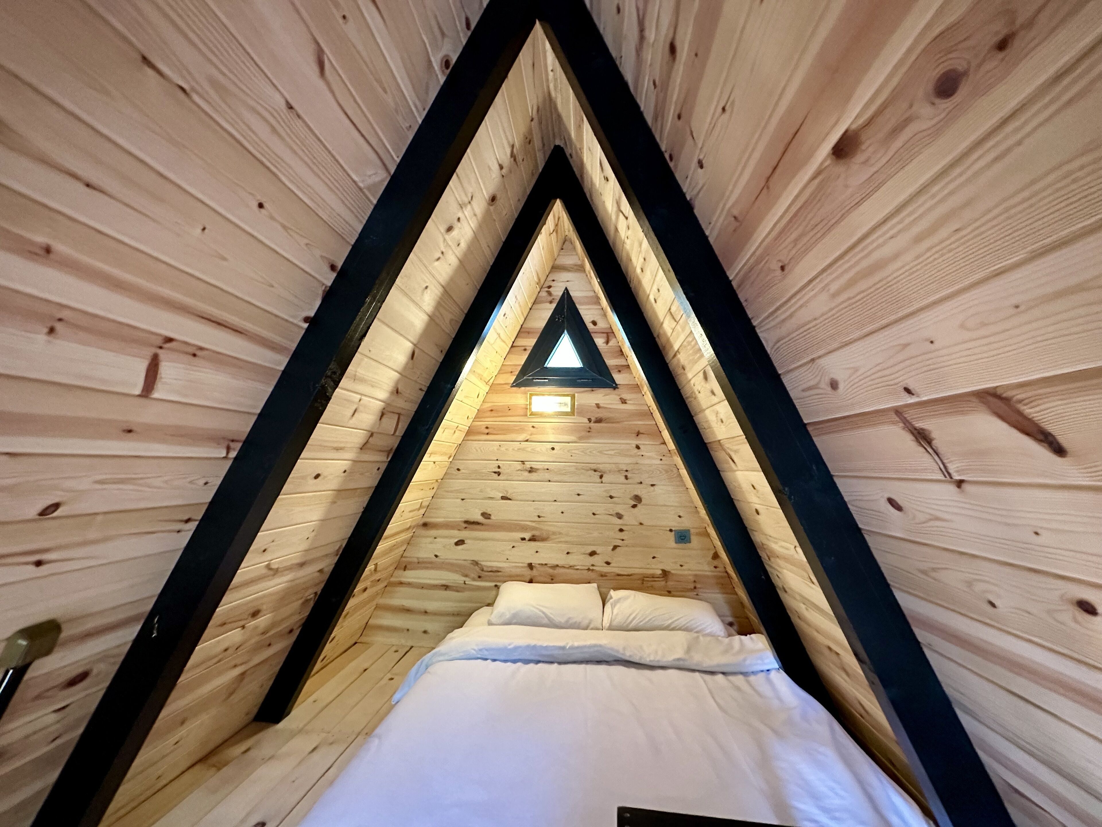 A triangular wooden room with a bed and a skylight.