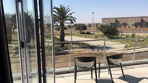 A balcony with two chairs, a view of a landscaped area with palm trees, and a building in the background. - Atlantic Apartments (Swakopmund)