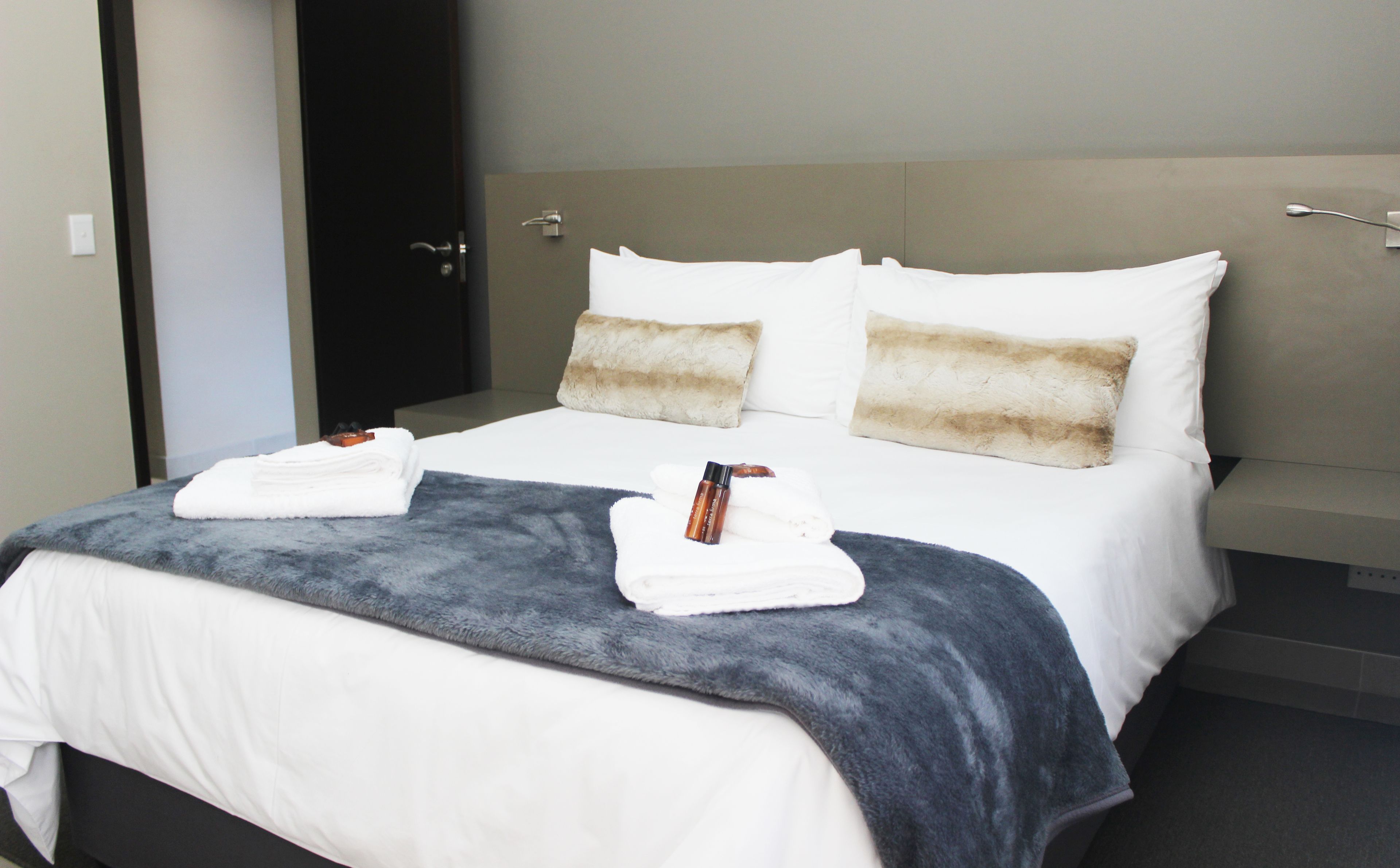 A neatly made bed with white and gray linens, a gray throw blanket, and two folded towels.
