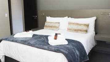A neatly made bed with white and gray linens, a gray throw blanket, and two folded towels.