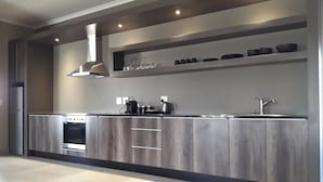 A modern kitchen with a built-in oven, a stainless steel range hood, and a countertop with a kettle and coffee maker. - Atlantic Apartments (Swakopmund)