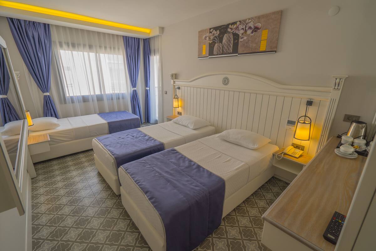 A hotel room with two beds, a desk, a chair, a lamp, and a painting on the wall.