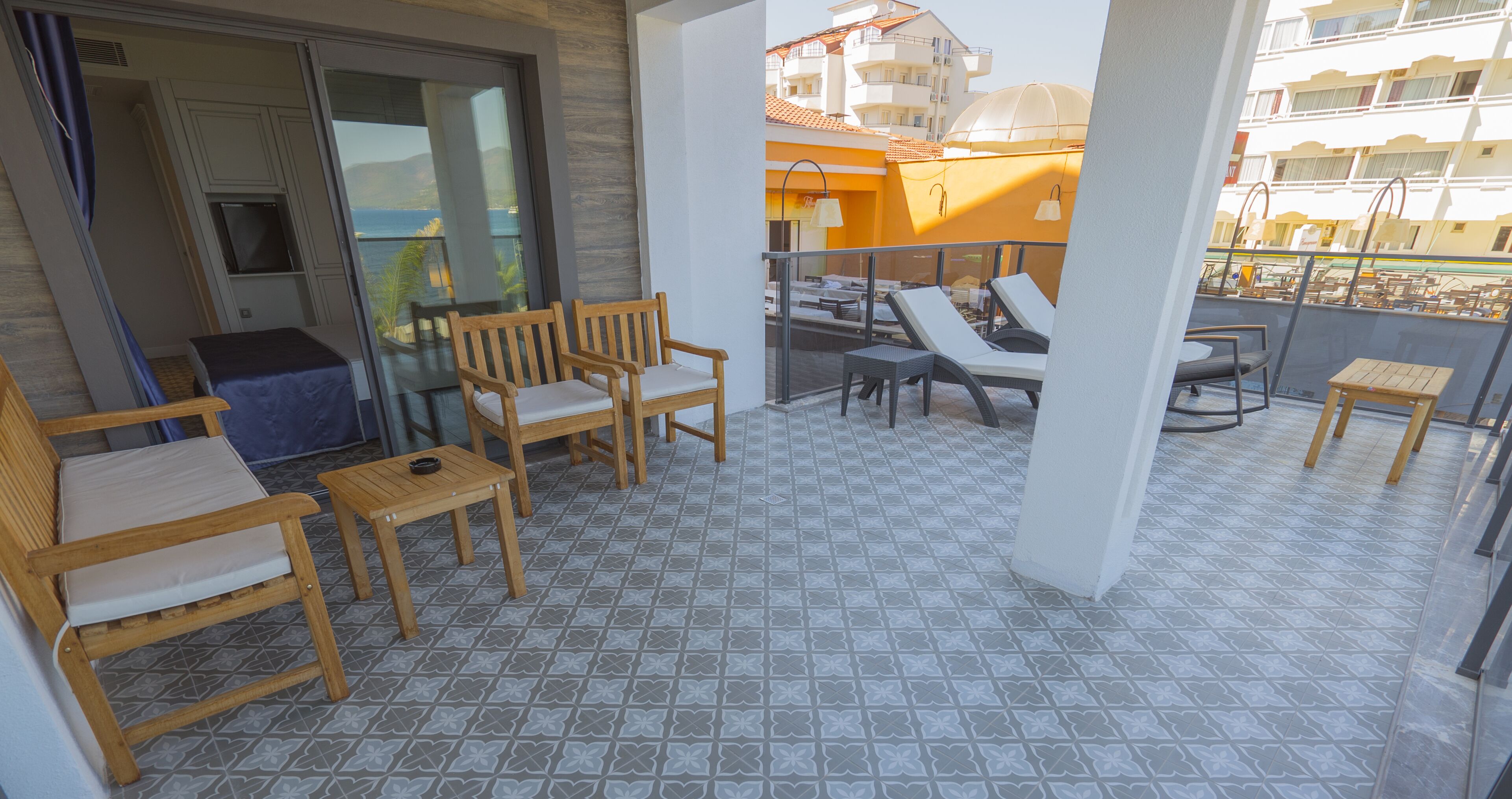 Ein Balkon mit Holzmöbeln, darunter Stühle und ein Tisch, und einem gemusterten Boden.