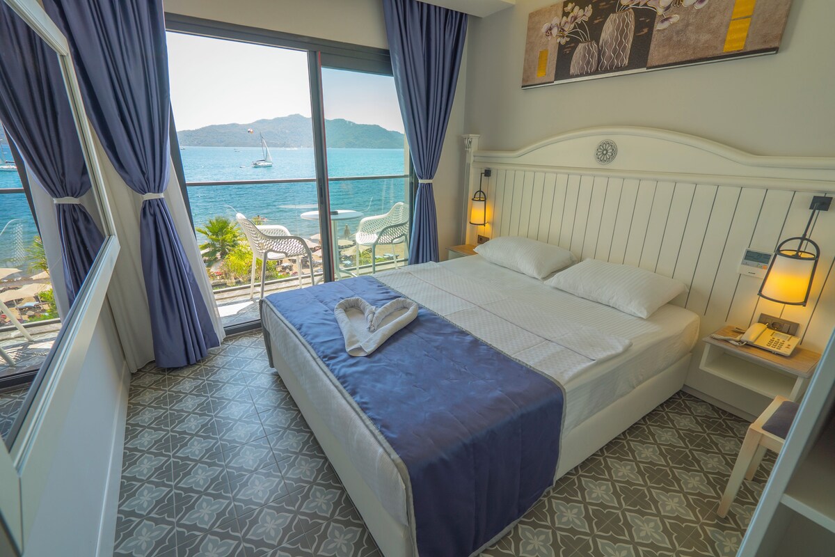 Ein Hotelzimmer mit Bett, Nachttisch, Lampe und Meerblick.