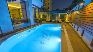 Una piscina con superficie de agua cristalina, rodeada por una terraza de madera y una barandilla de vidrio.