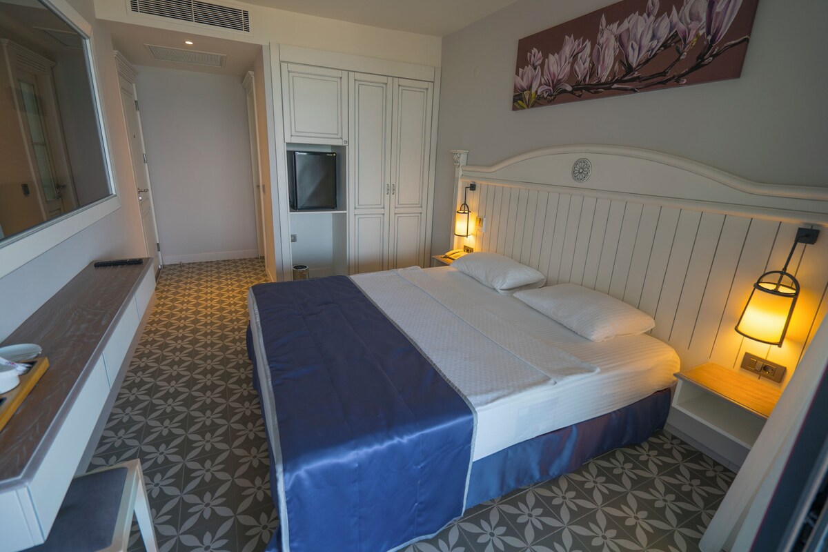 Ein Hotelzimmer mit Bett, Nachttischlampen, einem Fernseher und einem Bild an der Wand.