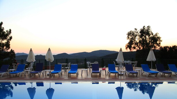 A poolside area with lounge chairs and umbrellas, reflecting the surrounding landscape. - Atlas Otel (Fethiye)