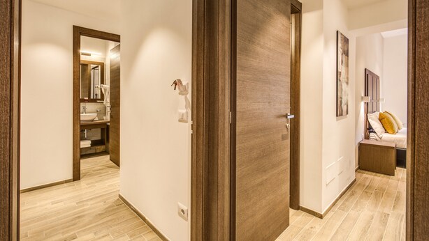 A modern hotel room with a wooden door, a bathroom with a sink and mirror, and a bed with pillows. - House Garden (Rome)