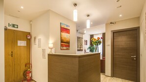 A reception area with a wooden reception desk, a fire extinguisher, and a wall-mounted sign. - House Garden (Rome)