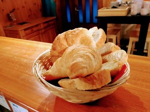 A wooden table with a glass bowl containing croissants and a red item, possibly a fruit.