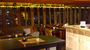 A restaurant interior with a table, chairs, and a view through large windows. - Pension du Lac Bleu (Evolène)