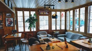A cozy restaurant with wooden interiors, large windows, and a mix of seating options including tables and sofas. - Pension du Lac Bleu (Evolène)