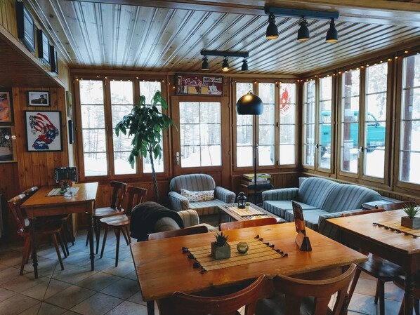 A cozy restaurant with wooden interiors, large windows, and a mix of seating options including tables and sofas. - Pension du Lac Bleu (Evolène)