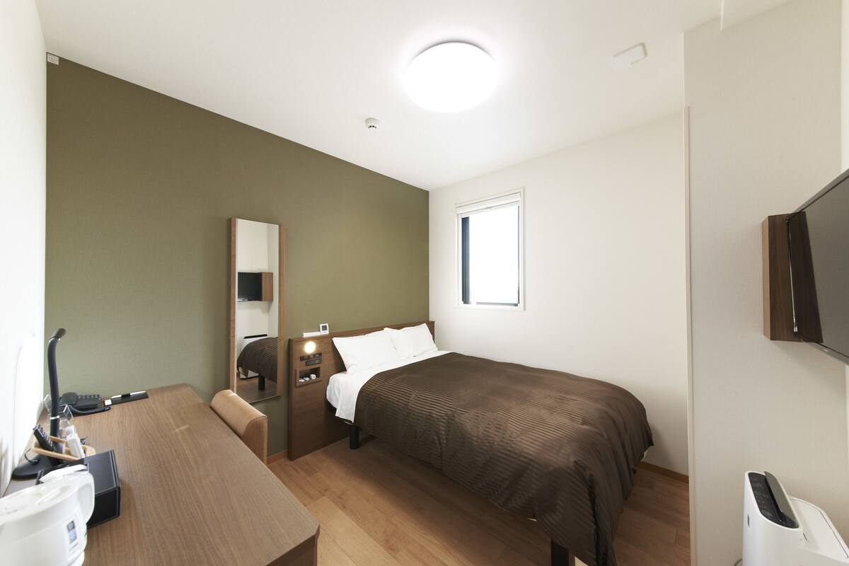 Une chambre d’hôtel avec un lit, un bureau, une chaise, une télévision et une fenêtre.
