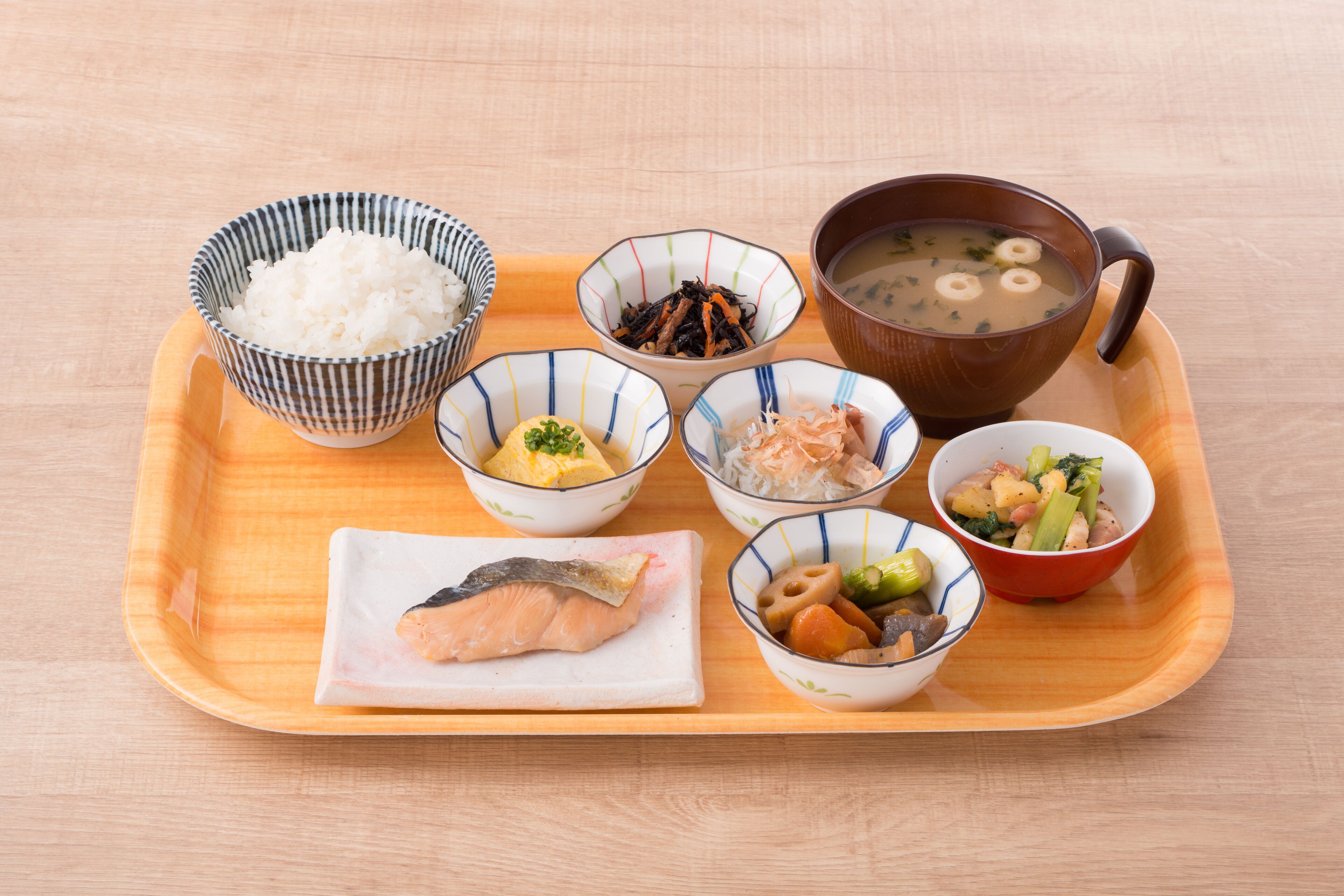 A wooden tray with various Japanese dishes including rice, fish, and soup.