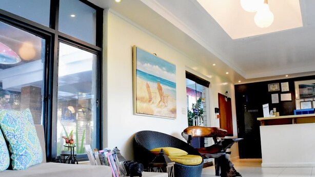 A modern hotel lobby with large windows, a reception desk, and a seating area with a sofa and chairs.