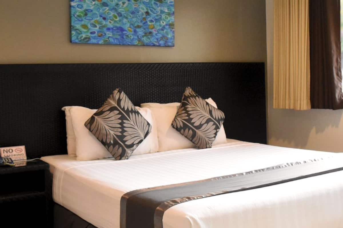 A neatly made bed with a black headboard, white bedding, and decorative pillows. A "No Smoking" sign is visible on a nightstand beside the bed.