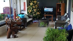 A spacious living area with a large potted plant, wicker furniture, and a television.