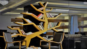 Una biblioteca moderna con una original estantería con forma de árbol, repleta de libros, rodeada de zonas de estar cómodas.