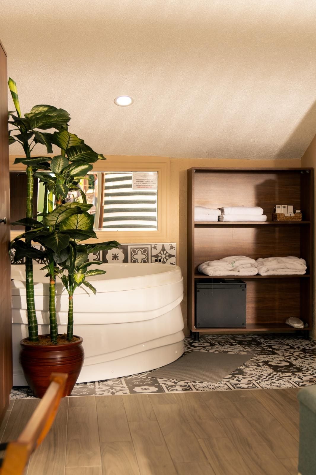 A bathroom with a curved bathtub, a potted plant, and a shelf with towels.