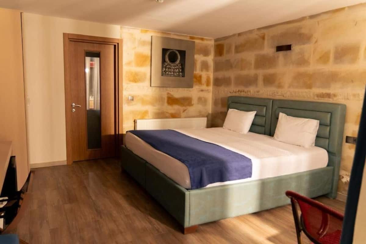 A bedroom with a bed, a door, a stone wall, and a framed picture.