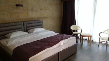 Ein Schlafzimmer mit einem Bett, zwei Stühlen, Holzboden und einem großen Fenster mit Vorhängen.