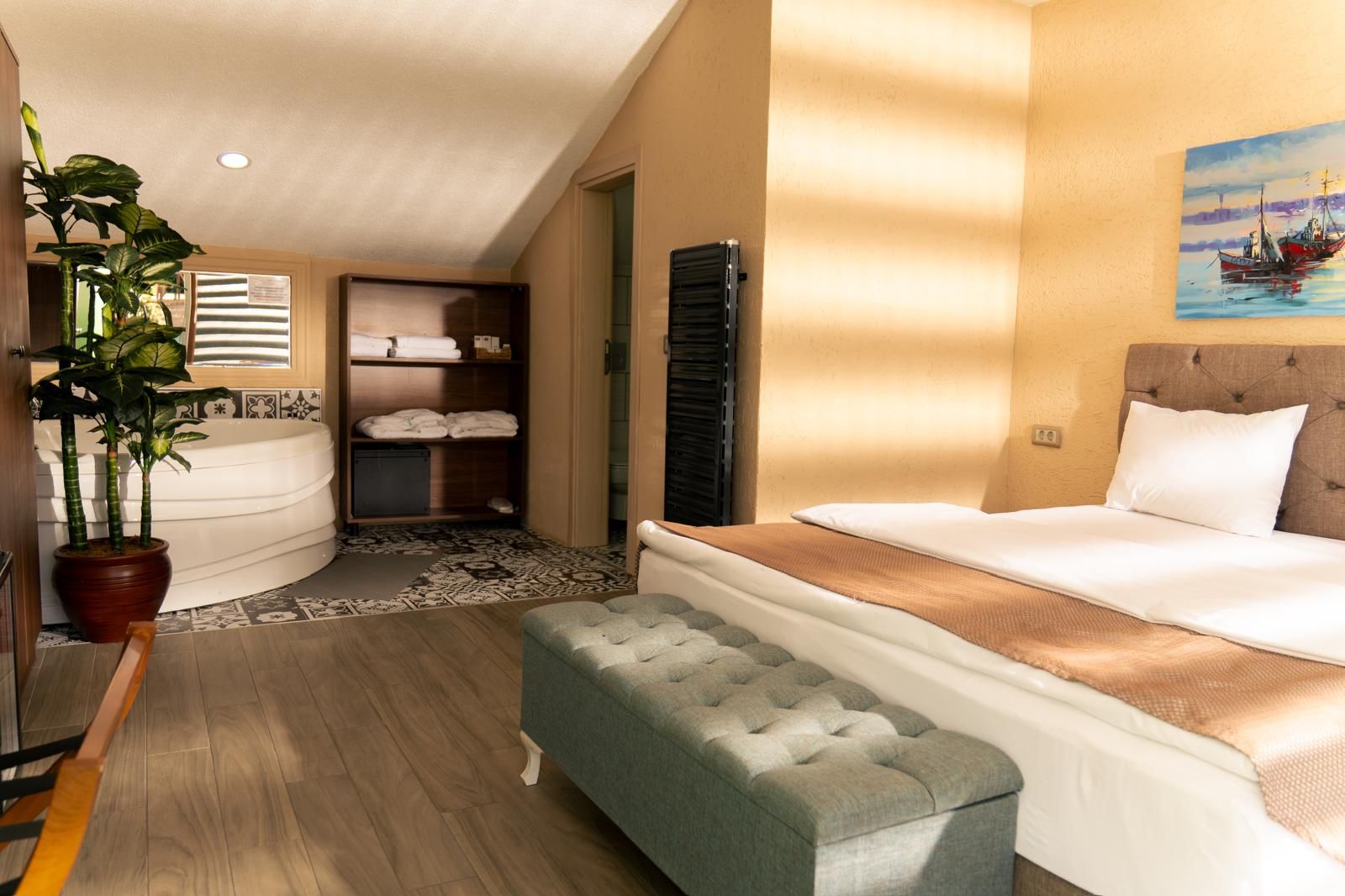 A hotel room with a bed, a seating area, a bathroom with a bathtub, and a potted plant.
