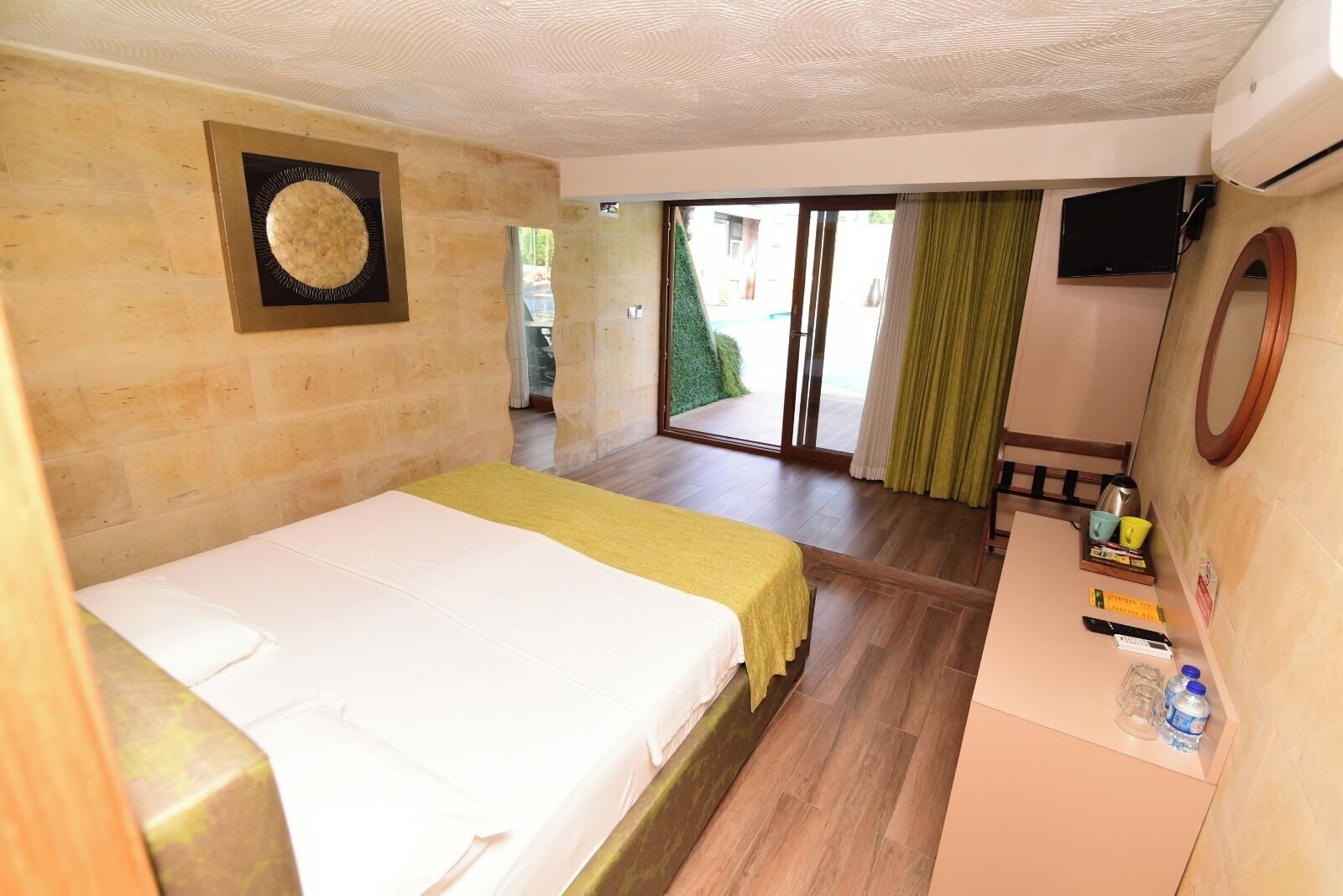 A hotel room with a bed, a desk with a mirror, a TV, and a view of the outside.