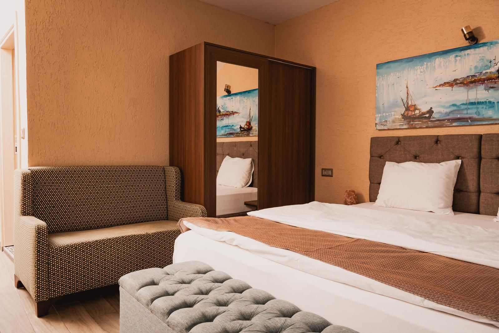 A hotel room with a bed, a sofa, a chair, and a painting on the wall.