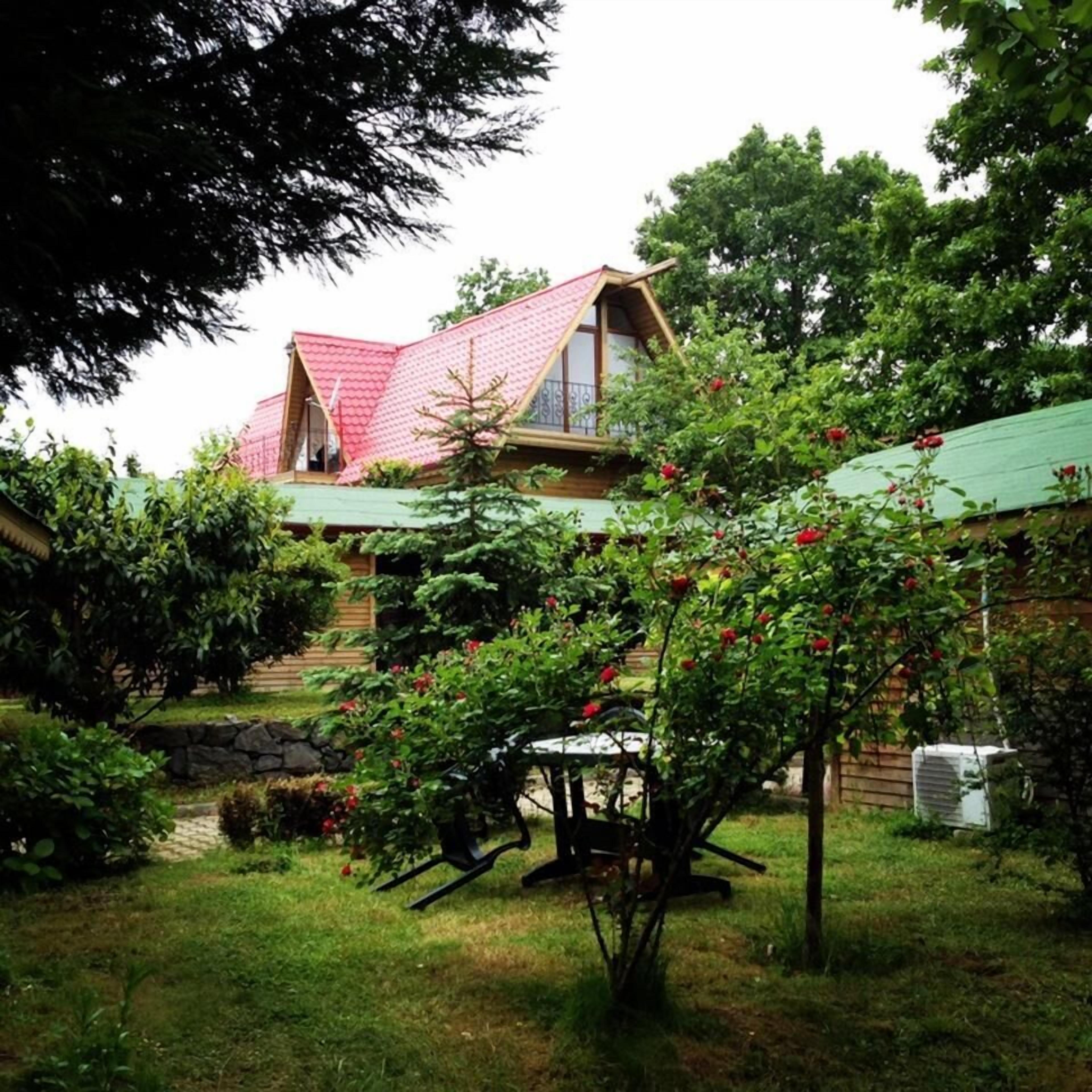 A house with a red roof, surrounded by lush greenery and flowering plants.