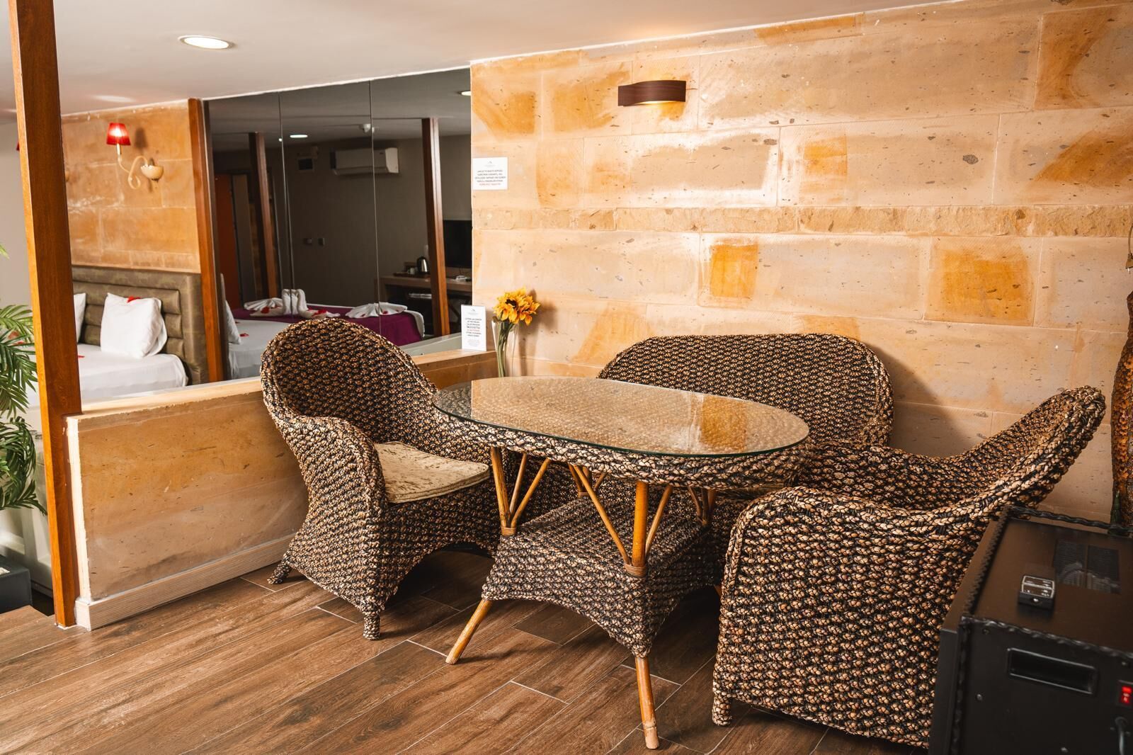 A room with a round glass table, wicker chairs, a brick wall, and a wooden floor.